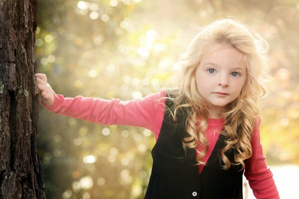 A girl with a wary look keeps one hand on the trunk of a tree