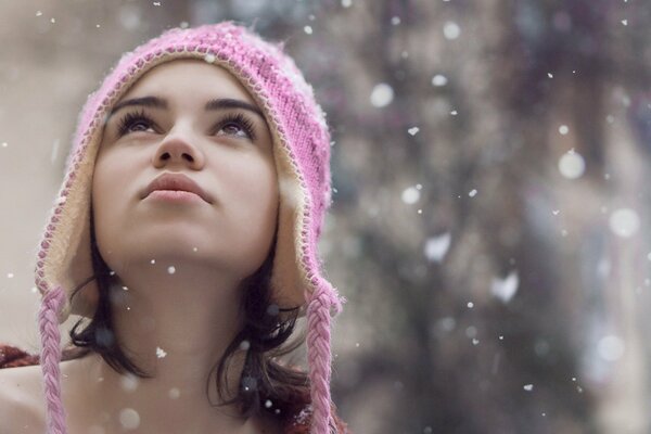 Fille dans un chapeau d hiver se penche sur les flocons de neige