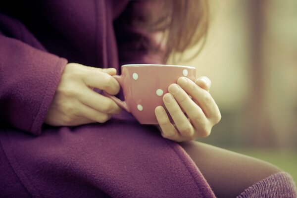 The girl warms her fingers on a cup of warm macro