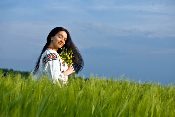 A girl is sitting in the grass with flowers in her hands