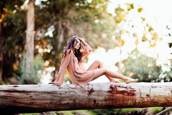 Beautiful girl on a log against a background of trees