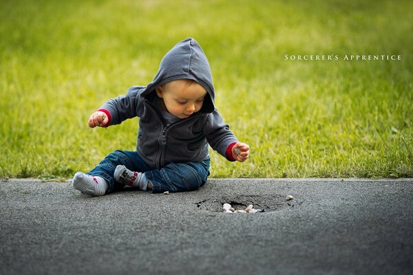 A boy on the street is sitting on the asphalt against the background of grass