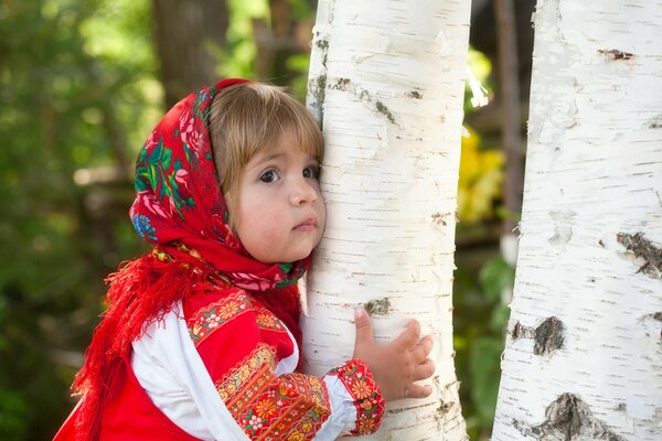 A girl in a scarf hugs a birch tree