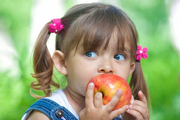 Ein Mädchen mit blauen Augen und Schwänzen isst einen Apfel