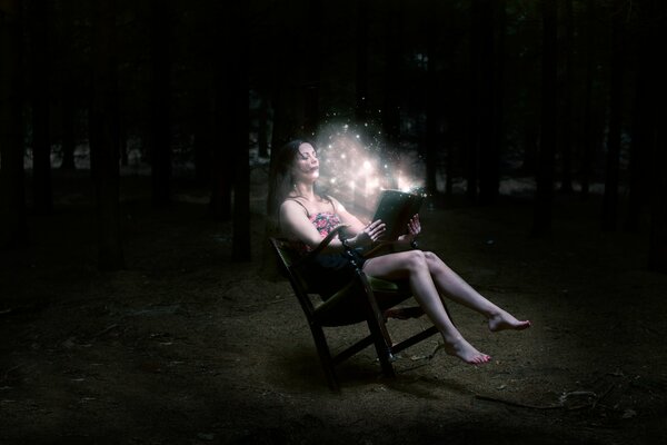 Chica de pelo oscuro se sienta en el bosque nocturno con un libro mágico