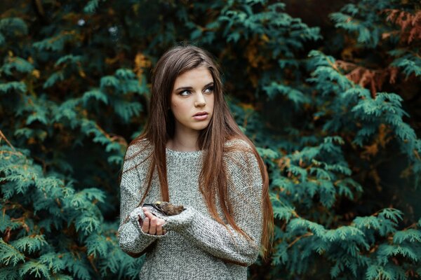 A girl in a sweater with a dead bird in her hands