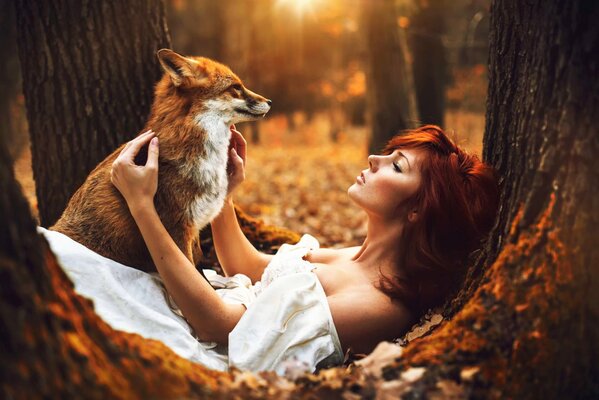 Red-haired girl posing with a fox in nature