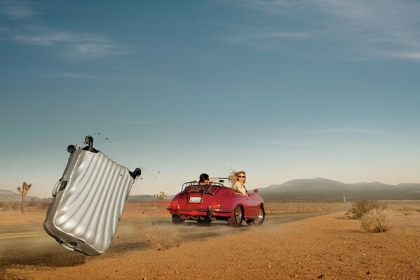 A suitcase fell out of a red car in the middle of the desert