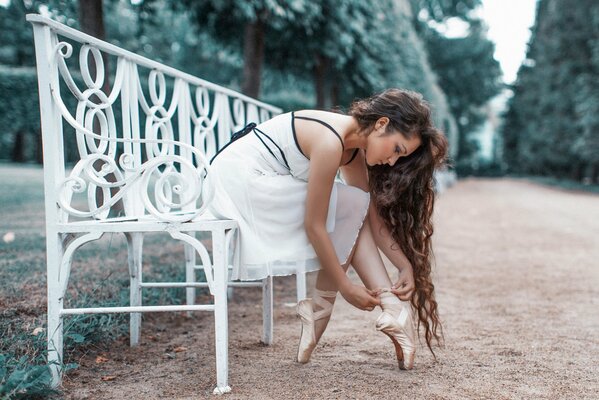 A girl wearing pointe shoes on a white bench in the park