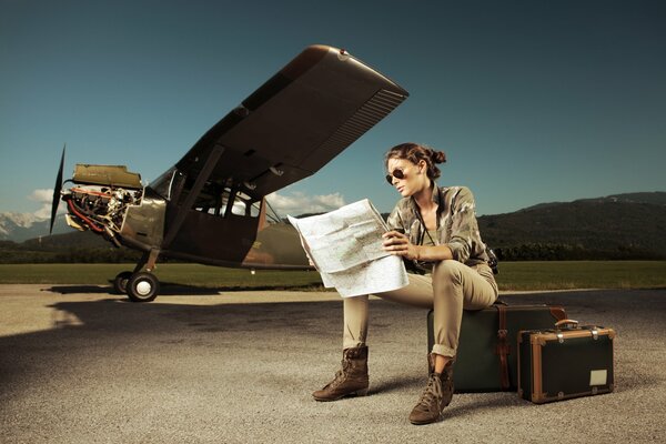 A girl with a map in her hands, sitting on suitcases next to the plane