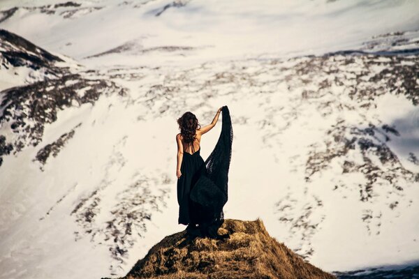 Chica en vestido negro en las montañas cubiertas de nieve