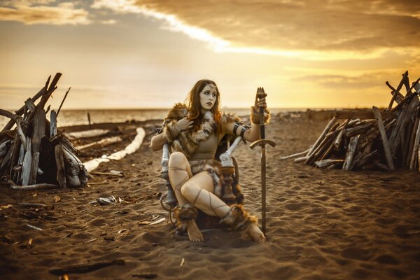 The girl is sitting on the shore with a sword in her hands