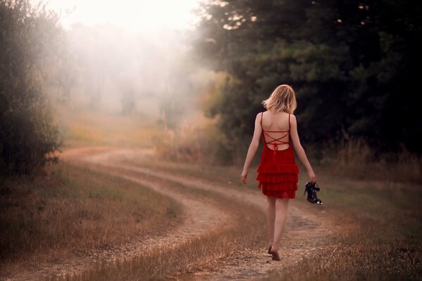 A barefoot girl in a red dress walks down the road