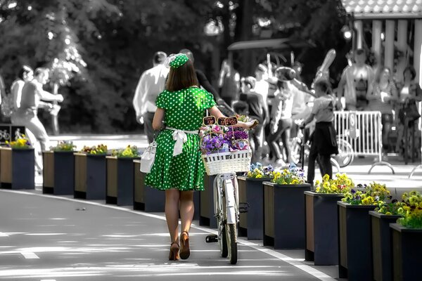 Ein Mädchen im grünen Kleid fährt ein Fahrrad mit Blumen