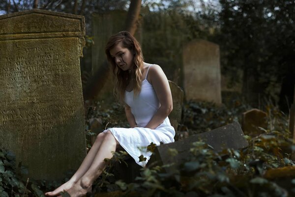 Weinendes Mädchen im weißen Kleid auf dem Friedhof am Grabstein