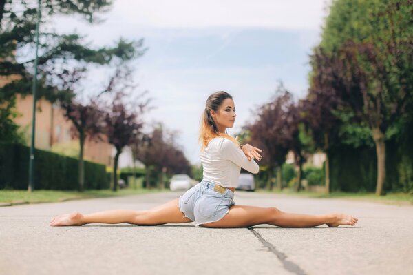 On the road, a girl in shorts does a stretching twine