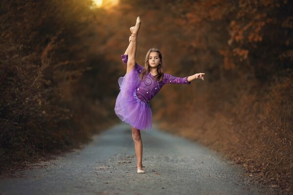 A girl in a purple tutu dancing in the woods