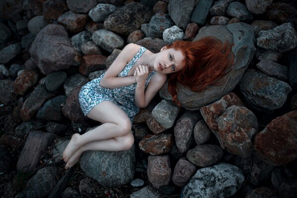 Chica pelirroja con pecas yace en una piedra fría