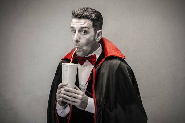 Ein Mann im Dracula-Kostüm trinkt Saft aus einem Röhrchen