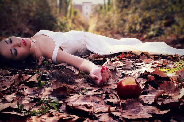 A beautiful girl lies on the foliage poisoned by a red apple