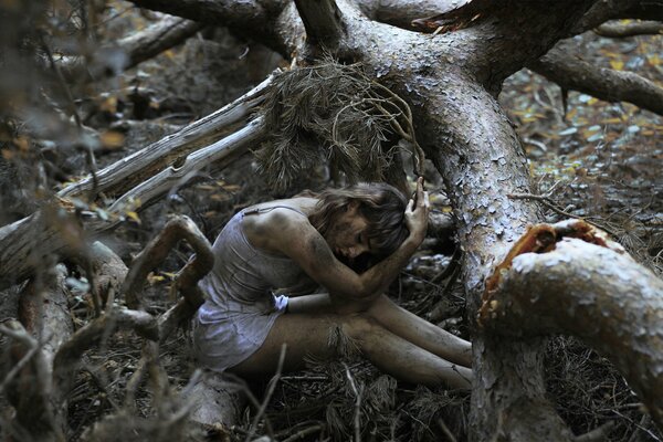 Bella ragazza seduta nella foresta sporca, intorno agli alberi