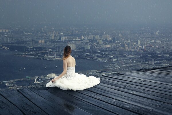 A girl is sitting on the roof of a tall building in the rain