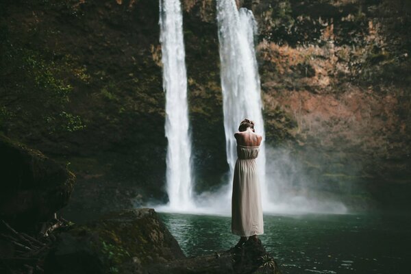 Chica de pie en el agua cerca de una cascada