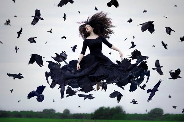 A girl in a black dress hovered above the ground in a flock of Ravens