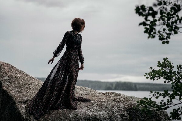 A girl in a beautiful dress on a stone next to the sea