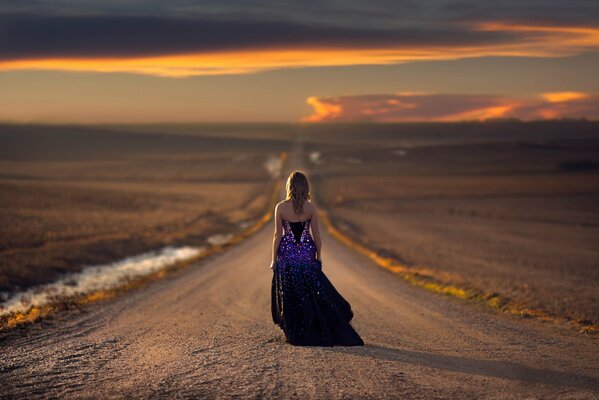 Fille marche sur la route au coucher du soleil dans une robe de soirée