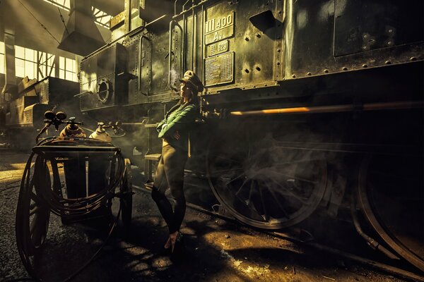 The girl stands by the locomotive and smokes