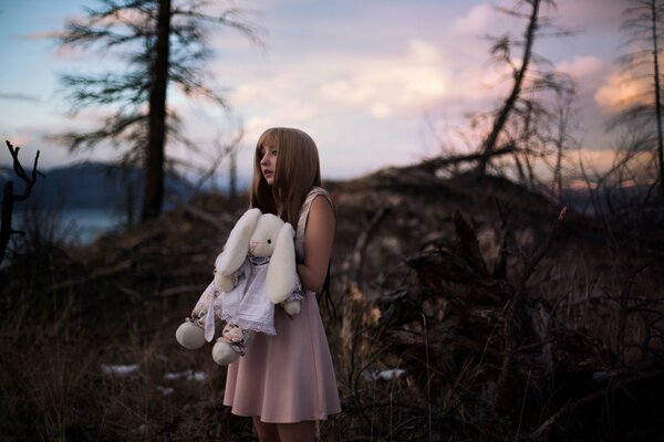 A girl in a dress in the forest holds a toy bunny