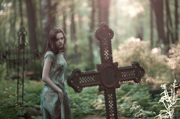 The girl looks at the cross in the cemetery