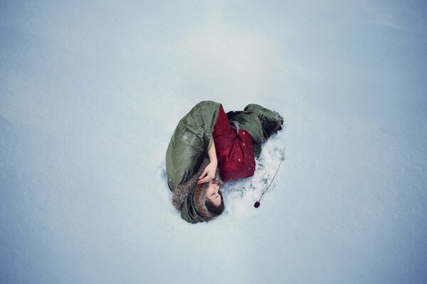 Das Mädchen liegt im Schnee neben einer roten Rose