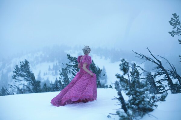 Mädchen in einem rosa langen Kleid, das durch den Schnee geht