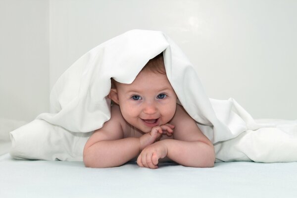 Bébé aux yeux bleus riant sous la couverture