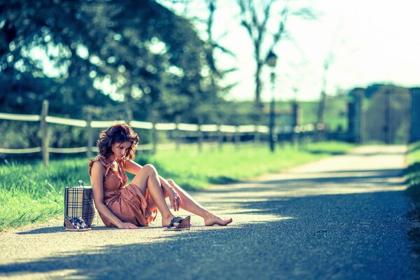 A girl in sandals is sitting with a bag on the road