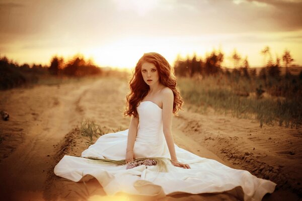 La jeune mariée dans une robe de mariée sur un chemin de sable. Autour des fleurs