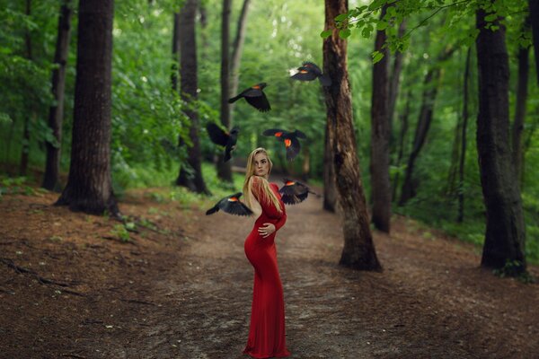 Una chica con un hermoso vestido de pie en medio del bosque rodeado de aves