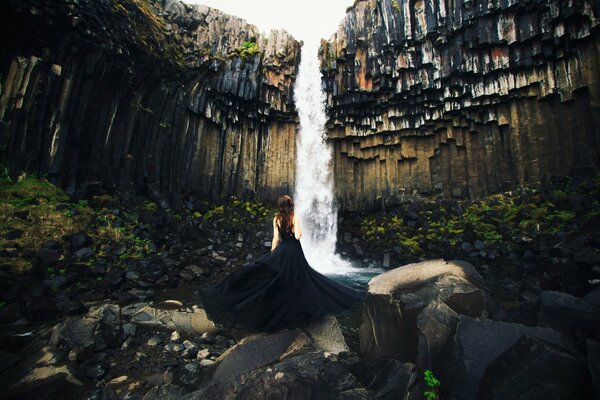 A girl in a black dress on the background of a waterfall