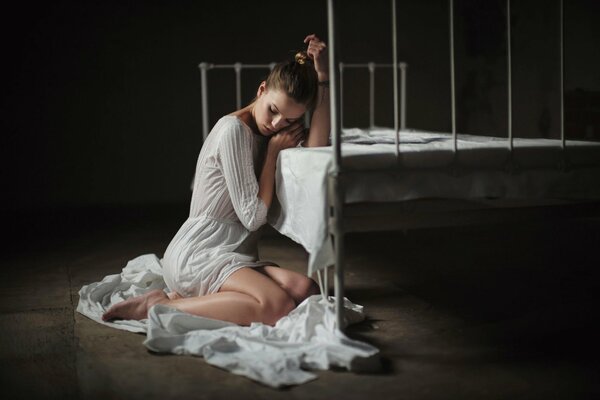 Ragazza in bianco sul pavimento accanto al letto