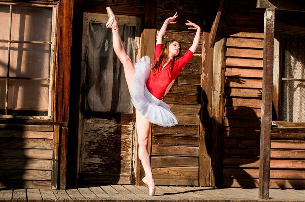 A ballerina dances against the background of a wooden house