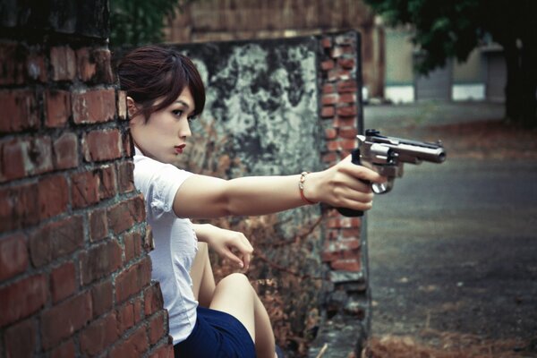 Asian woman with a gun near a brick wall