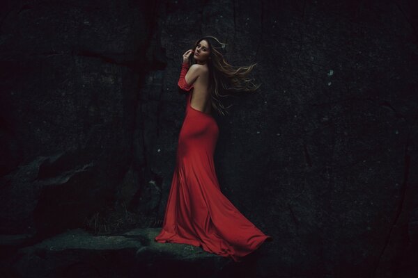 Belle fille en robe rouge avec dos ouvert sur fond de roche sombre