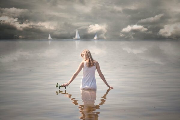 La chica está de pie en el agua. Velas en el mar