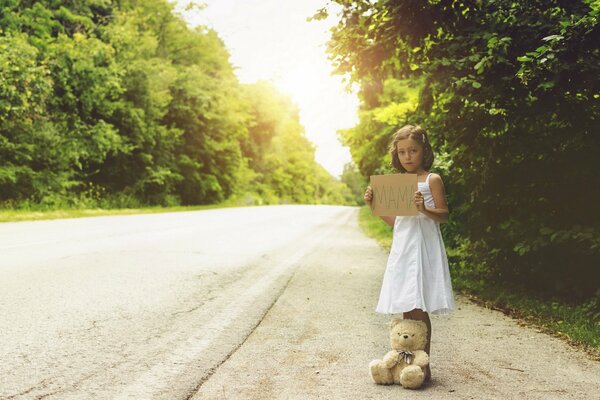 A little girl with a bear is standing in the middle of the road