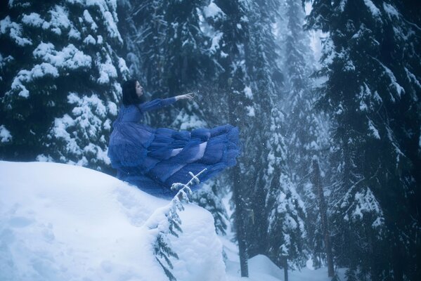 Una chica con un vestido azul sobre un fondo de abetos en la nieve