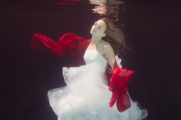 Chica en vestido blanco con bufanda roja bajo el agua