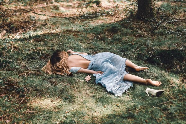 A girl in a dress without shoes is lying on the grass