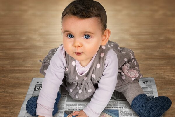 A little girl is sitting on a newspaper